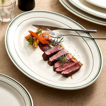 Oval porcelain steak plate with grilled steak and vegetables on a warm dining table.