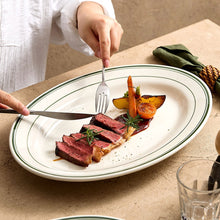 Hands plating steak and roasted vegetables on an oval porcelain serving plate.