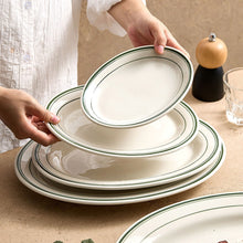 Stacked oval porcelain plates with a fine green line rim on a dining table.